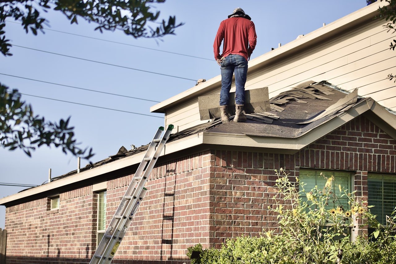 Roofer working on the roof of a brick home with a ladder set up